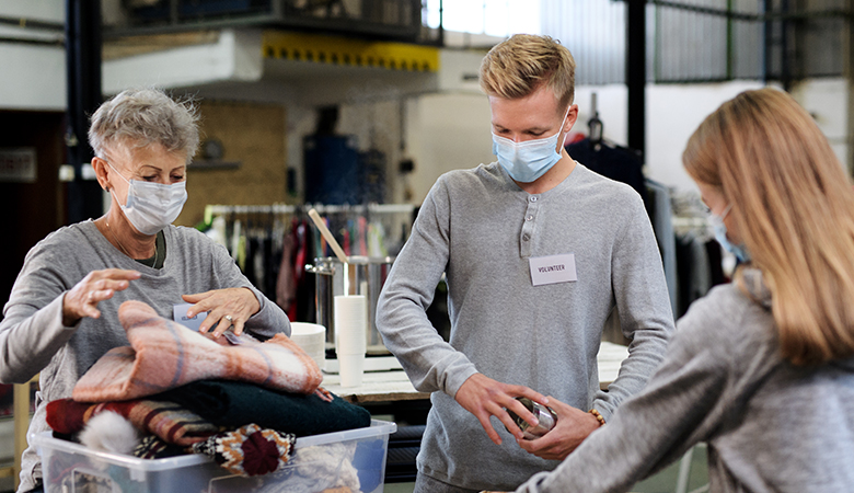 Drei junge Menschen helfen einer älteren Person beim Packen von Kisten mit Lebensmitteln und Kleidung in einer sozialen Einrichtung.