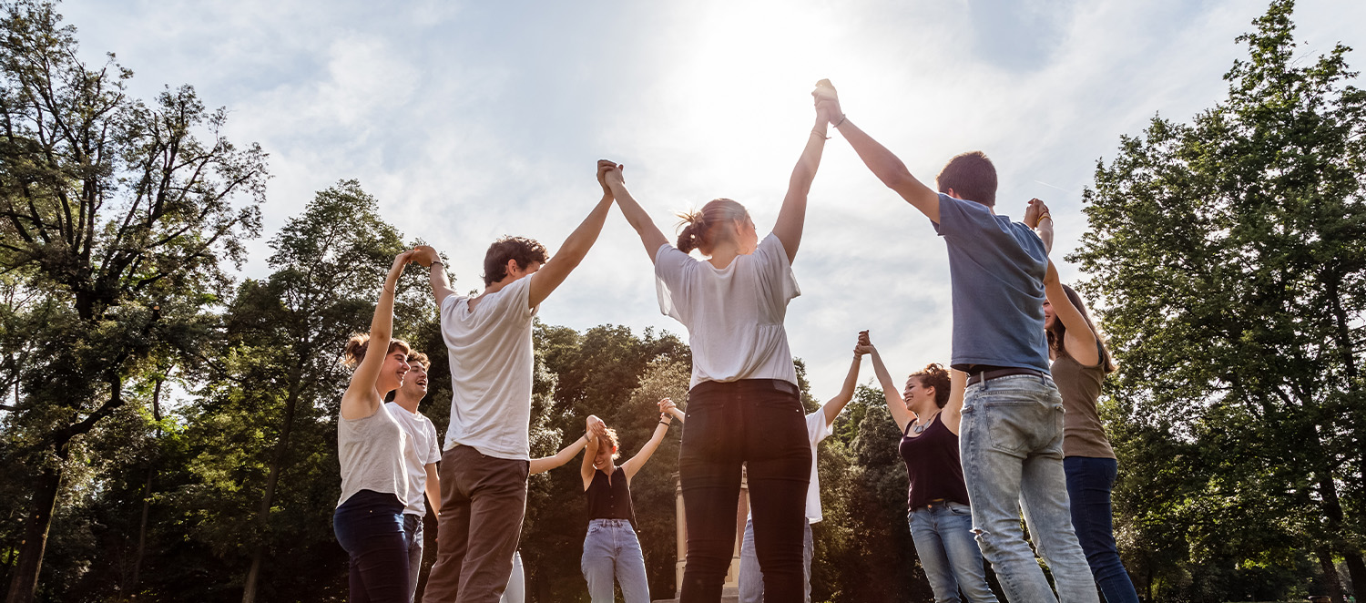 Eine Gruppe von jungen Menschen steht im Kreis und hält sich an den Händen. Sie stehen auf einer Wiese.